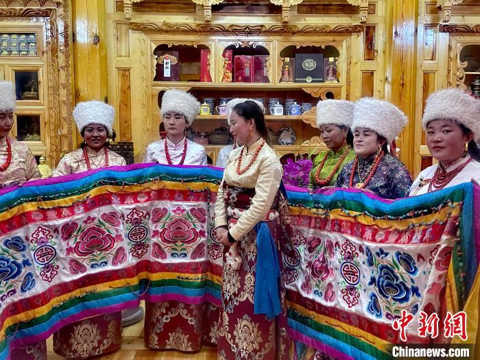 圖為女性展示村民自發(fā)繡制的“百米五彩哈達(dá)”?！±钣穹?攝